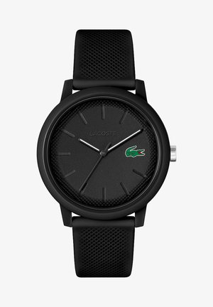 Ceas Lacoste negru cu un cadran texturat, ace argintii și accent cu logo. Curea moale din silicon cu un model. Design minimalist.