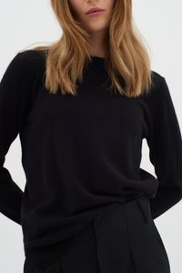 Pulover negru tricotat cu mâneci lungi, decolteu rotund și textură moale, asortat cu pantaloni negri cu talie înaltă. Design simplu, fără modele.