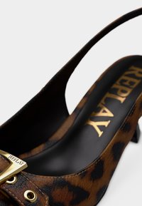 Πέδιλο slingback με λεοπάρ σχέδιο, γυαλιστερό μαύρο εσωτερικό, χρυσές μεταλλικές λεπτομέρειες και υφή στην εξωτερική επιφάνεια. Το ύψος της φτέρνας είναι περίπου 2 ίντσες.