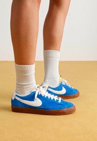 Zapatillas de ante azul con el swoosh blanco de Nike, diseñadas con un perfil bajo y suelas de goma marrón, combinadas con calcetines blancos de punto.