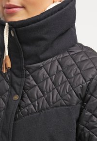 Veste bleu marine en mélange de laine avec un panneau matelassé en nylon noir, col haut, cordon de serrage en corde et accent en cuir sur la fermeture.