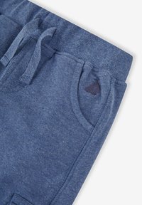 Blå sweatpants i mjukt material, med dragsko i midjan, sidofickor och en liten marinblå logotyp nära fickan.