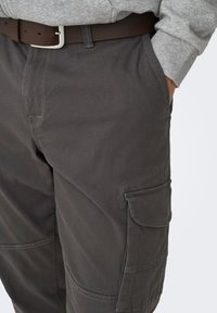 Pantalones cargo grises hechos de tela duradera, con múltiples bolsillos, un ajuste relajado y un cinturón de cuero marrón.