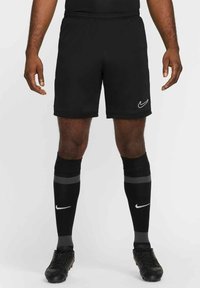 Zwarte Nike sportshorts met een elastische tailleband, gedragen met zwarte kniekousen met grijze strepen en een wit logo, en zwarte voetbalschoenen.