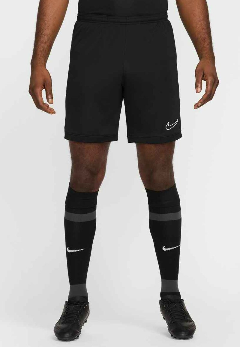Zwarte Nike sportshorts met een elastische tailleband, gedragen met zwarte kniekousen met grijze strepen en een wit logo, en zwarte voetbalschoenen.
