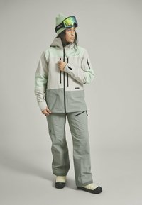 Lightweight, two-tone ski jacket in mint green and grey with zippers, paired with matching trousers and cream-colored footwear.