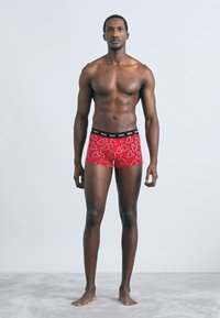 Piros boxeralsó szívmintával, fekete derékpánttal, testhezálló kialakítással és puha anyaggal. A modell magabiztosan áll semleges háttér előtt.