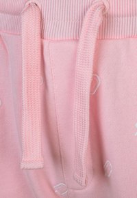 Rosa Sweatpants mit weichem Textil, geripptem Bund und gewebten Kordeln. Auffällige dekorative Akzente sind entlang des Stoffes sichtbar.