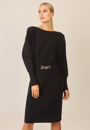 Schwarzes geripptes Strickkleid mit einem Boot-Ausschnitt, langen Ärmeln und einer figurbetonten Silhouette. Verfügt über einen metallischen Kettenakzent an der taillierten Taille.