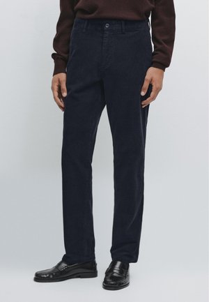 Pantaloni in velluto a coste blu navy con taglio dritto, dotati di chiusura con bottone e tasche laterali, abbinati a mocassini neri lucidi.