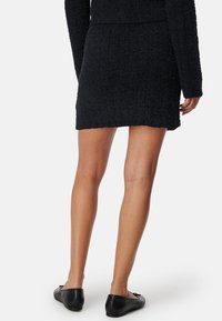 Mini-jupe noire texturée au design ajusté, associée à des chaussures plates noires. Présente un tissu doux côtelé et un ourlet net.