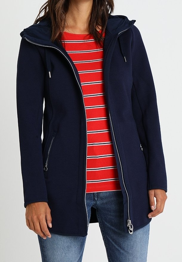 Laivastonsininen vetoketjullinen takki hupulla, jossa sivutaskut, teksturoitu kangas ja hopeanväriset yksityiskohdat. Päällä punaraitainen paita.