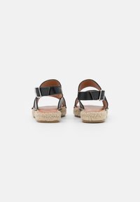 Sandali in pelle nera con suole in juta stile espadrille, cinturini alla caviglia regolabili e design del retro arrotondato. Texture liscia con accenti naturali.