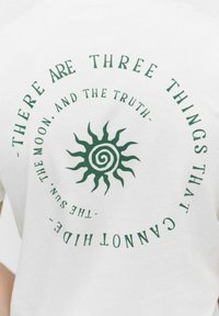 Hvid t-shirt med et grønt spiral sol-grafik og teksten "DER ER TRE TING, DER IKKE KAN GEMME SIG - SOLEN, MÅNEN OG SANDHEDEN."