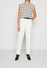 Superior de manga corta a rayas en blanco y negro, combinado con pantalones blancos de talle alto y botas de tobillo negras y puntiagudas. Diseño simple con colores sólidos.