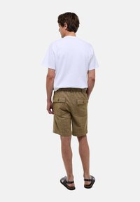 T-shirt blanc à manches courtes associé à un short en kaki texturé doté de deux poches arrière et d'une taille élastique. Des sandales noires complètent la tenue.