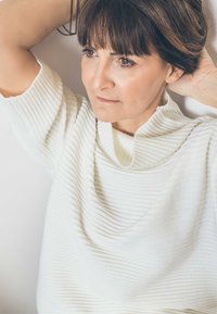 Rippierter, cremefarbener Pullover mit einem fallenden Kragen und kurzen Ärmeln. Glattes, strukturiertes Material auf einem hellen Hintergrund.