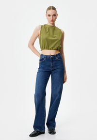 Przycięty oliwkowozielony top bez rękawów z marszczonym dołem, połączony z wysokim stanem niebieskich dżinsów w fasonie dzwonów i czarnymi butami. Prosty design, teksturowana tkanina.