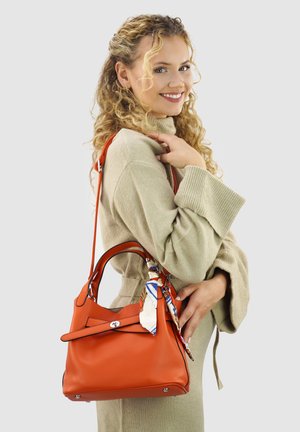 Orangefarbene Lederhandtasche mit einer strukturierten Form, die eine Schleifenakzent und ein angebrachtes gemustertes Halstuch aufweist. Die Tasche hat zwei Griffe und silberne Beschläge.