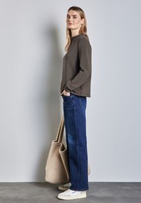 Felpa grigia scura, jeans a gamba larga blu e borsa tote beige con texture. Le sneakers bianche completano l'outfit. Design semplice e casual.