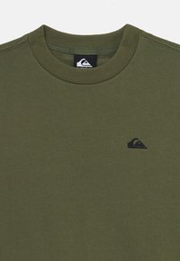 Olivovo zelený oversize sveter s okrúhlym výstrihom vyrobený z mäkkej tkaniny, s malým čiernym logom na hrudi a rebrovanými manžetami a výstrihom.