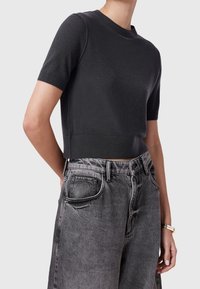 Svart kortärmad croppad tröja i slät tyg, i kombination med högmidjade, bleka grå jeans i denim med fickor och bälte.