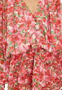 Bloemenjurk met roze, rode en groene bloemblaadjes, voorzien van stoffen knopen aan de voorkant en gelaagde rimpeldetailen in de rok.