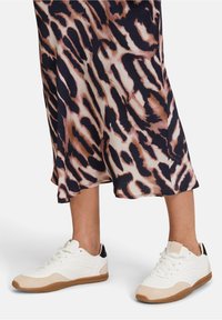 Baskets blanches avec des accents en suède beige et un contrefort de talon noir, associées à une jupe fluide ornée d'un imprimé animal marron et crème.