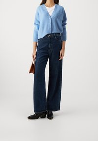 Jasnoniebieski prążkowany kardigan z dekoltem w serek i guzikami, zestawiony z wysokim stanem ciemnych dżinsów o szerokich nogawkach oraz czarnymi botkami na klocku.