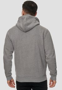 Sweat-shirt gris avec une texture douce, présentant une grande capuche, des poignets côtelés et une coupe légèrement ajustée, vu de dos.
