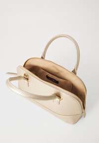 Sac à main métal doré au design structuré, fermeture zippée et deux anses courtes. L'intérieur présente une doublure beige et une étiquette de marque.