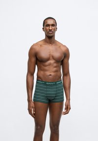 Zöld-fehér csíkos férfi boxeralsó GANT logós derékpánttal. Pamut anyagból, testhezálló kialakítású, a comb közepéig érő hosszúságú.