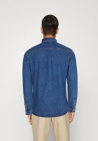 Jeansskjorta med en mörkblå finish, knäppta manschetter, klassisk krage och ryggveck, med rak skärning och slät textur.