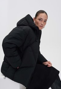 Doudoune noire avec capuche, présentant un design matelassé et un rembourrage épais. Le tissu a l'air brillant avec une texture lisse.