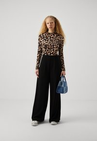 Long-sleeve leopard print top paired with high-waisted black trousers. Holding a small blue handbag, featuring smooth texture and angular shape.