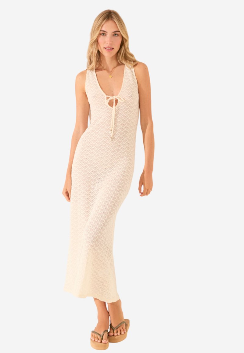 Robe maxi en tricot crème avec un motif en chevrons, décolleté en V et détail de noeud ajustable au niveau de la poitrine. Modèle associé à des sandales à plateforme.