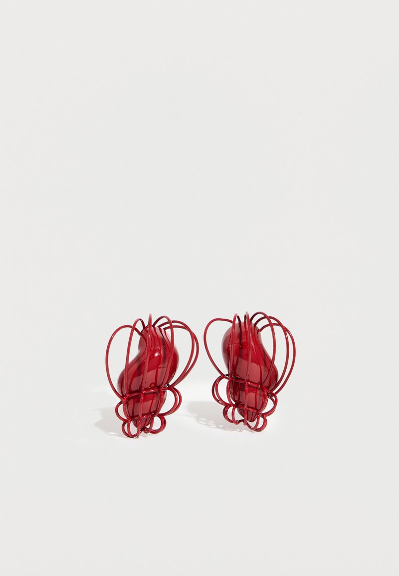 Dve rdeči abstraktni žični skulpturi z gladkimi, zaobljenimi središči na belem ozadju, ki mečeta mehke sence.
