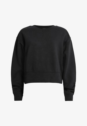 Kobieta w czarnej bluzie z haftem złotych węży na ramionach, czarnej mini spódnicy cekinowej ze złotymi wzorami węży i czarnych workowatych botkach.