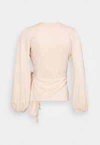 Blusa de cor creme com mangas longas e bufantes, detalhe de cintura atada e um tecido liso, ligeiramente elástico. Decote redondo simples nas costas.