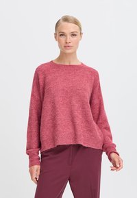 Pullover rosa a maglia con colletto rotondo, spalle cadenti e polsini a coste. Texture morbida con taglio leggermente corto e orlo grezzo.
