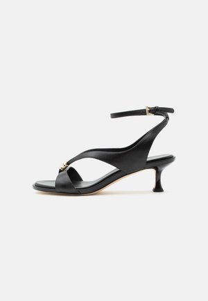 Sandale noire en cuir pour femme avec un petit talon courbé, des lanières croisées et une bride de cheville réglable avec une petite boucle dorée.
