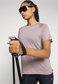 Hele lilla sportline T-särk lühikeste varrukatega, tekstuuriga kangas, kantud mustade matkakeppidega, millel on hall käepide ja rihm.