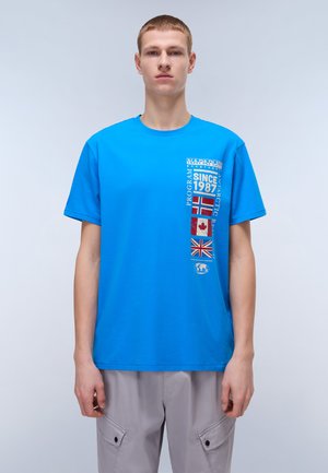 Blå bomulds t-shirt med korte ærmer, der har grafiske designs og flag, herunder Norge og Canada, på venstre front.