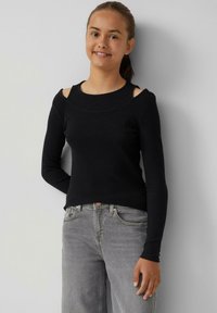 Schwarzes, geripptes Langarmoberteil mit ausgeschnittenen Schultern. Es hat einen runden Halsausschnitt und wird mit grauen Jeans kombiniert.