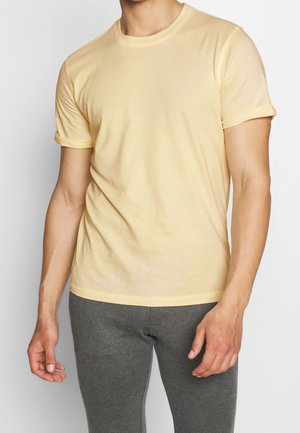 T-shirt en coton jaune à manches courtes avec un col rond et des manches légèrement retroussées, associé à un pantalon gris ajusté. Texture lisse.