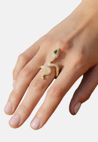 Bague en or en forme de serpent avec un œil en pierre précieuse verte, ornée de petites cristaux transparents, présentant un design flexible qui s'enroule autour du doigt.