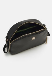 Borsa a mano in pelle sintetica nera con forma arrotondata, cerniere dorate e dettaglio del logo. Presenta due scomparti e una finitura testurizzata.