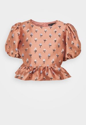 Blouse en satin pêche avec des manches bouffantes et un imprimé floral bleu et blanc. Elle présente un col rond et un ourlet volé.