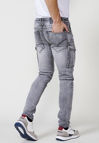 Grijze denim jeans met een slim fit, meerdere zakken en contrasterende stitches. Gecombineerd met grijze en witte sneakers.