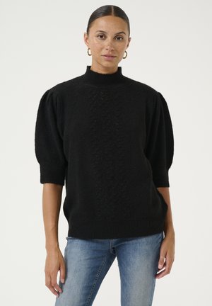 Schwarzer gestrickter Pullover mit einem hohen Kragen, puffigen kurzen Ärmeln und einem strukturierten Muster in der Mitte, kombiniert mit hellblauen Jeans.
